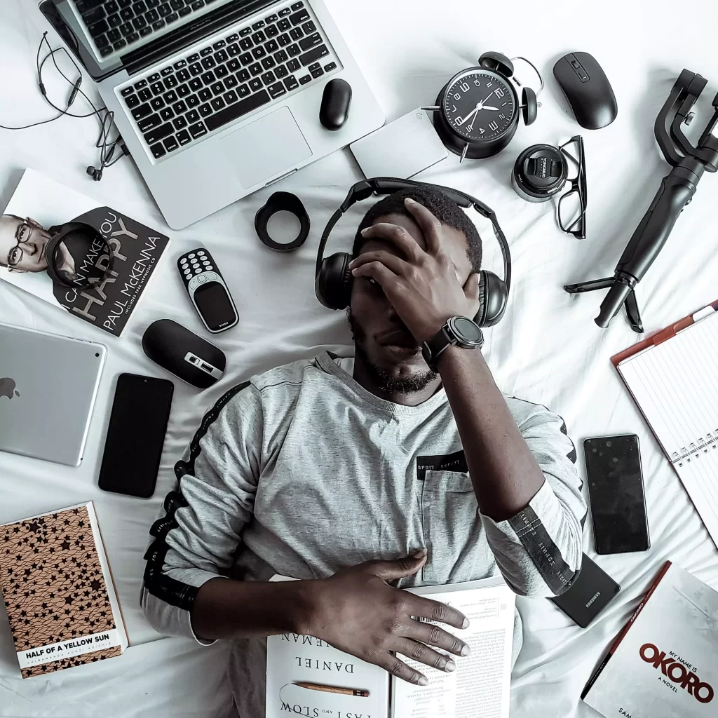 A man is laying wearing headphones and electronic devices are spread around him